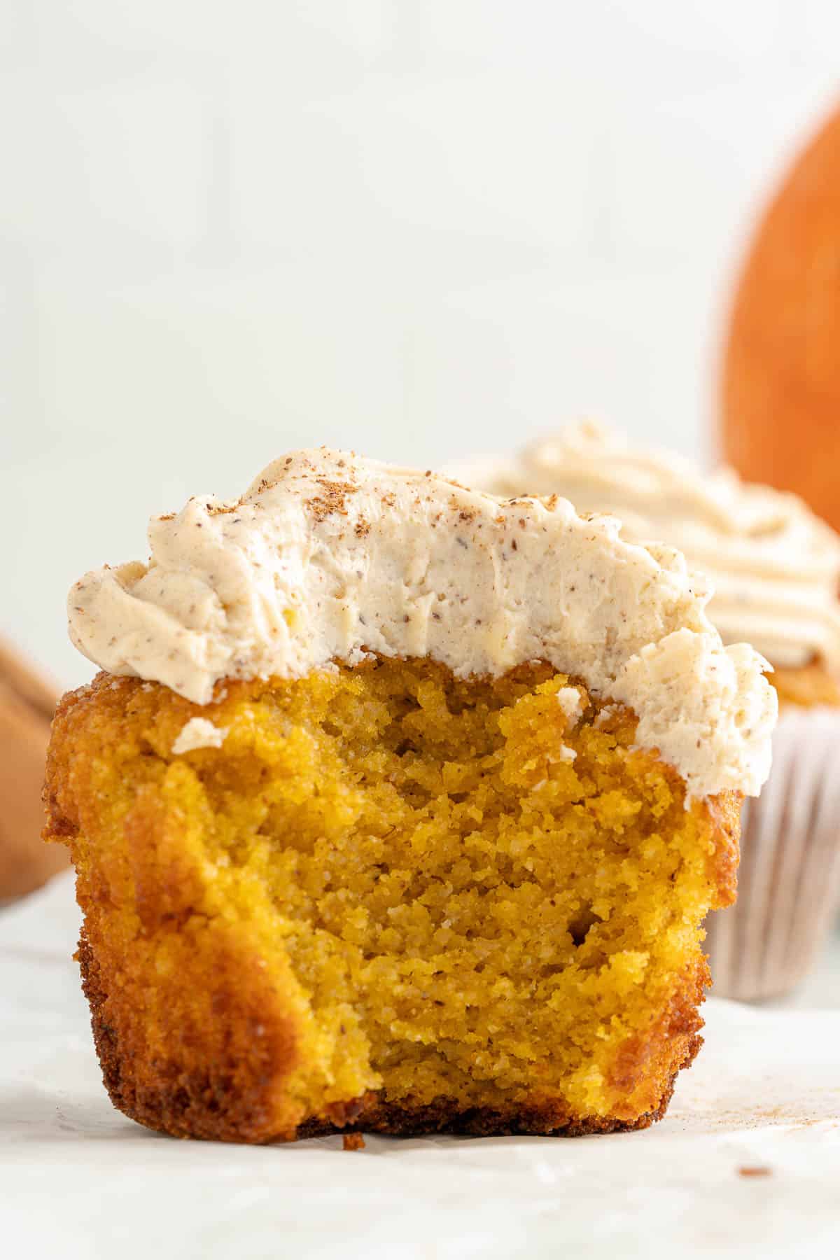 A wooden cutting board with low carb pumpkin cupcakes, topped with cream cheese frosting and sprinkled with cinnamon.