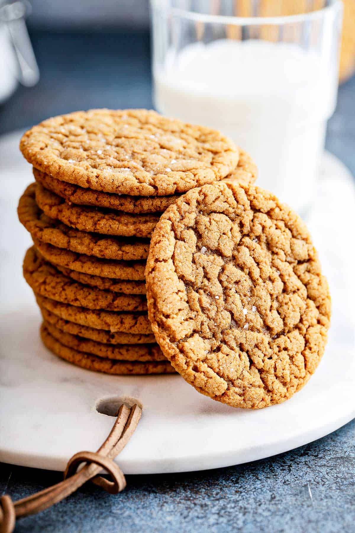 A tall stack of fresh baked gingersnap cookies on a marble serving platter, with a glass of milk.