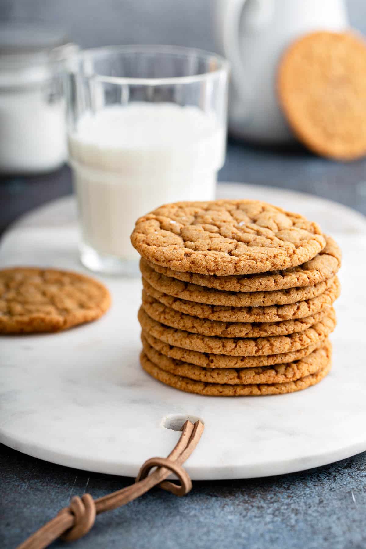 a stack of freshly backed gingersnap cookies on a white marble serving platter, with a glass of milk.