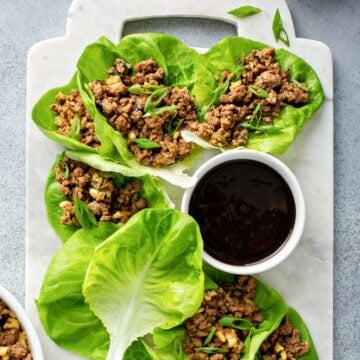 a white marble serving dish, topped with lettuce leaves, stuffed with an asian chicken mixture, served with soy sauce.