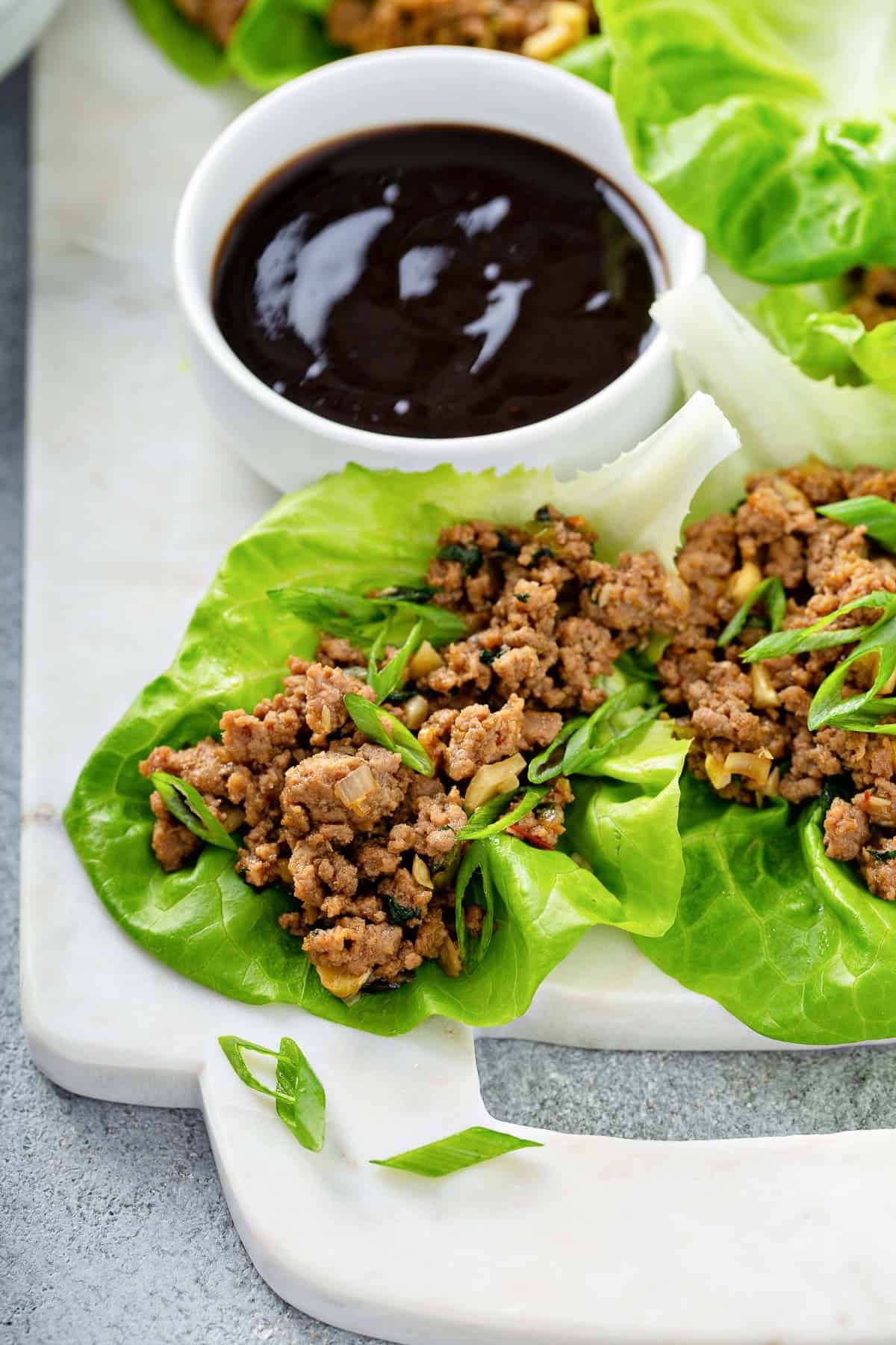 a white marble serving dish, topped with lettuce leaves, stuffed with an asian chicken mixture, served with soy sauce.