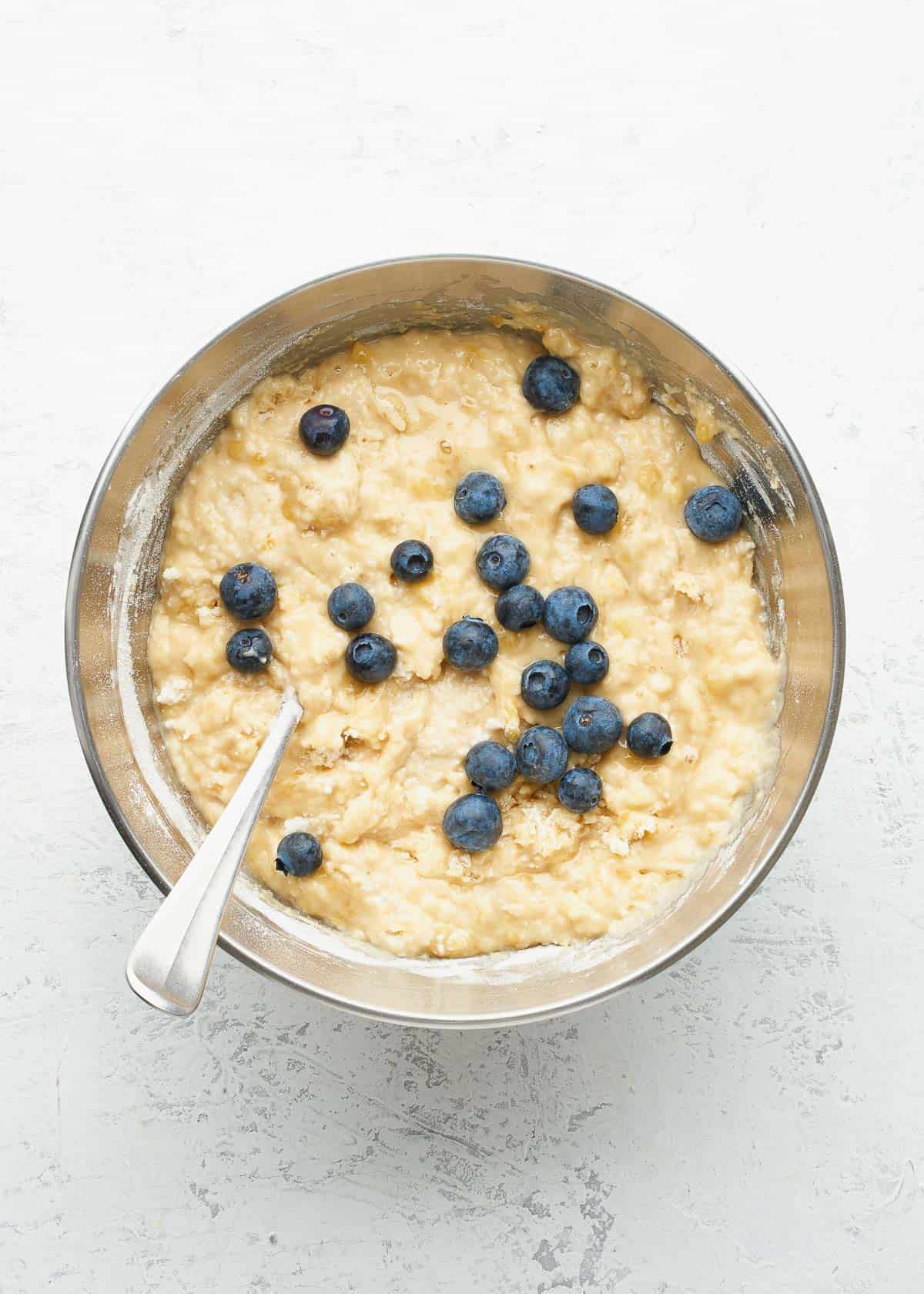 A mixing bowl full of banana bread batter with blueberries on top.