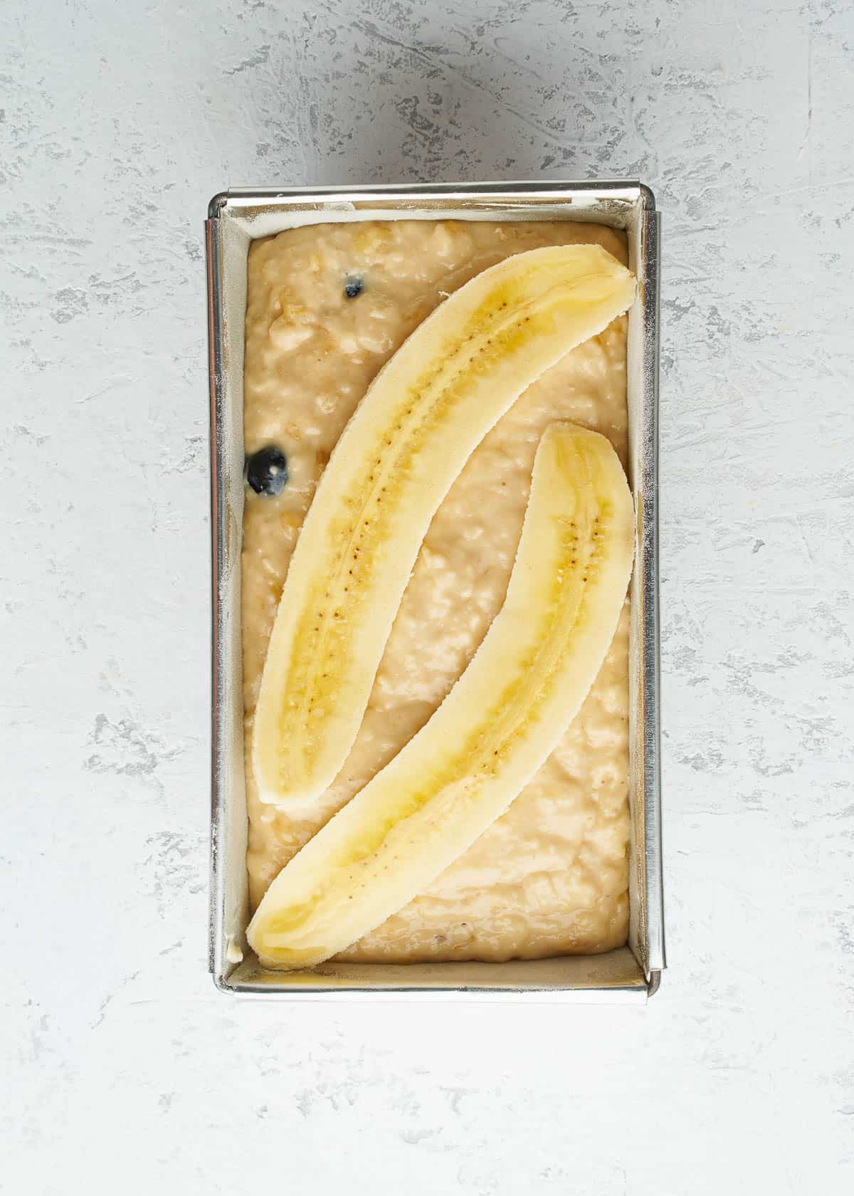 A loaf pan full of batter to make a blueberry banana bread, with a whole banana on top.