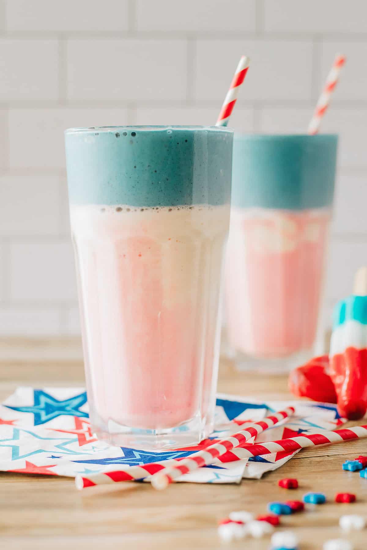 2 layered milkshakes - red, white, and blue, topped with whipped cream and sprinkles.