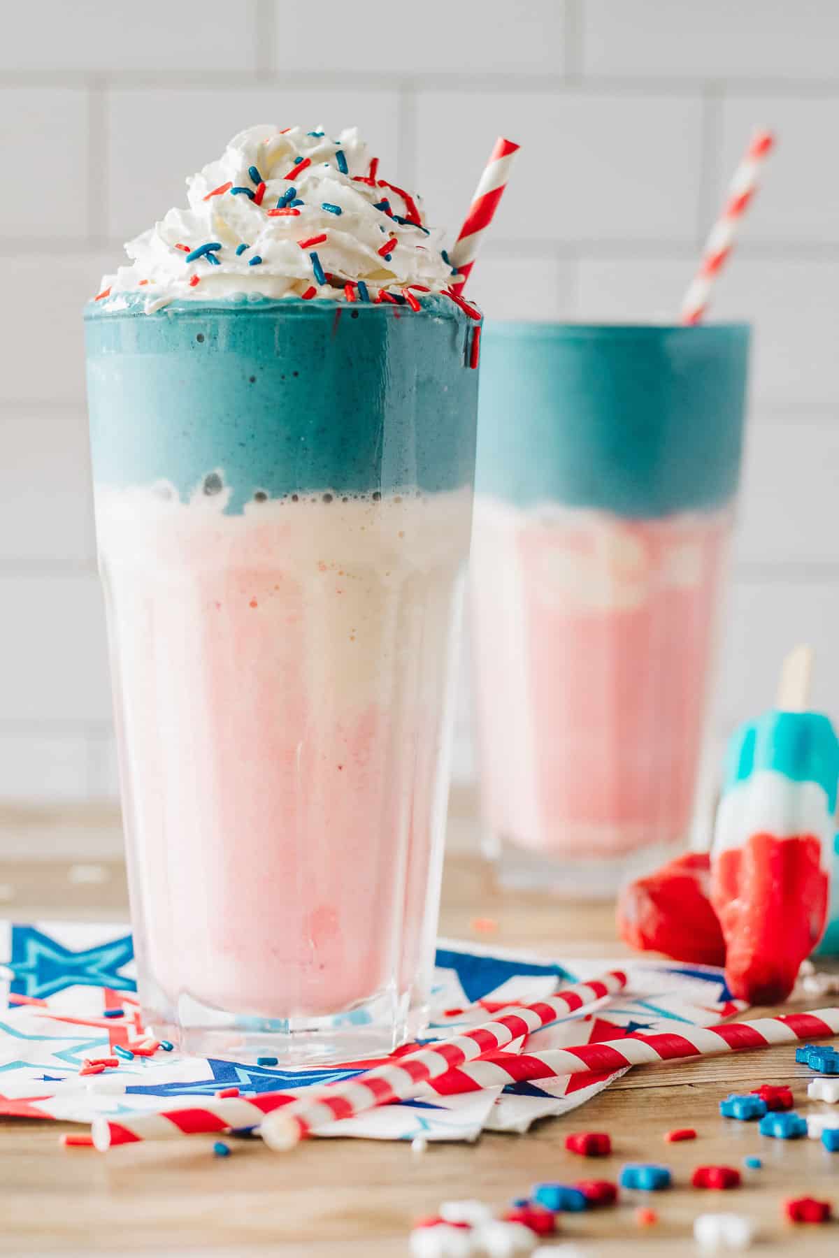 2 layered milkshakes - red, white, and blue, topped with whipped cream and sprinkles.