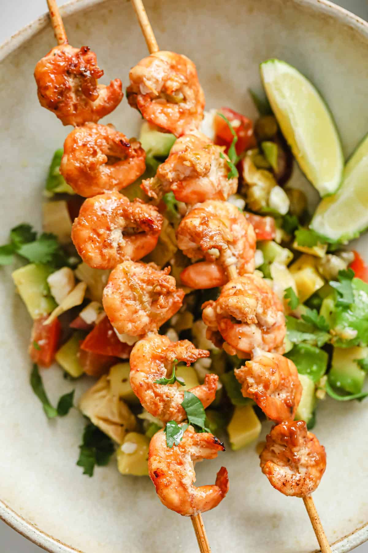 Grilled shrimp on a skewer, nestled on top of a fresh avocado salsa.