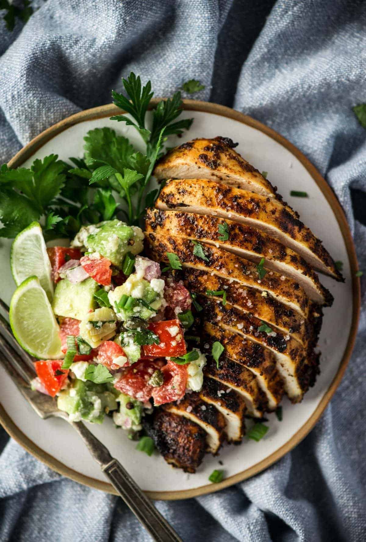 A grilled chicken breast, seasoned and sliced, served alongside salsa, cilantro and limes.