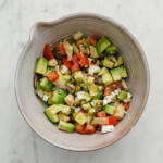 A ceramic bowl full of a salsa made with avocado, tomato, garlic, red onion, caper, artichoke hearts, and feta.