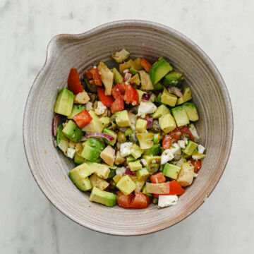 A ceramic bowl full of a salsa made with avocado, tomato, garlic, red onion, caper, artichoke hearts, and feta.