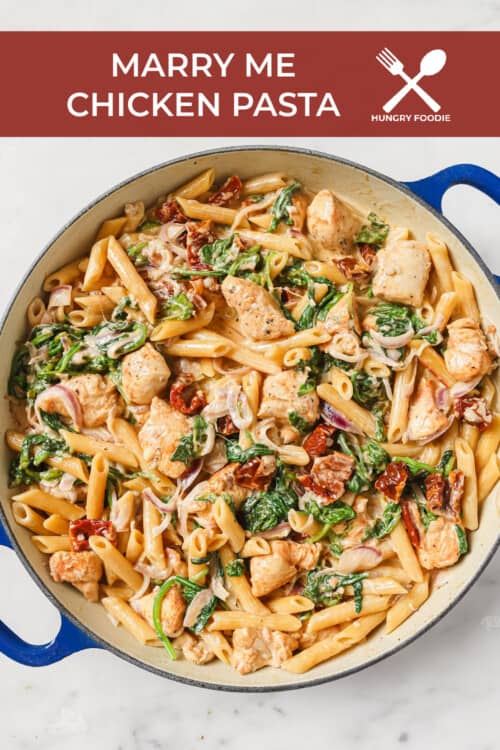An enameled cast iron skillet filled with a pasta dish made with chicken, penne, sun-dried tomatoes, spinach, red onion and a rich creamy sauce