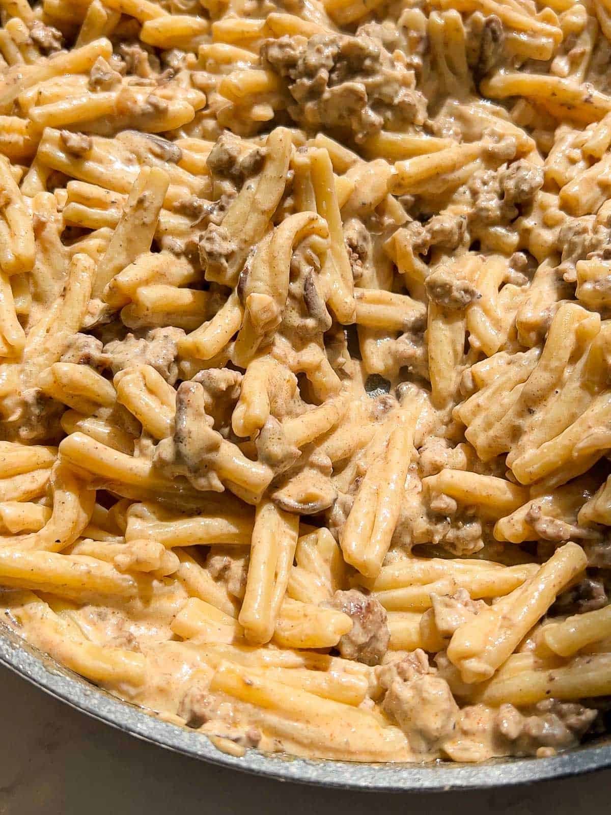 A large pan with a pasta dish made with ground beef, mushrooms, onions, and a sour cream sauce.