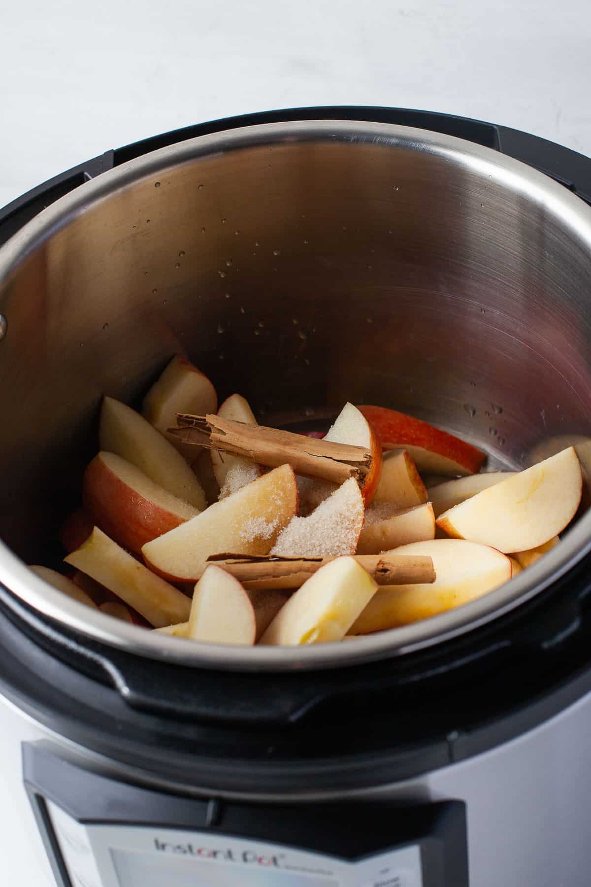 An Instant Pot with apples, vanilla, sugar, water, cinnamon and orange juice in it. 