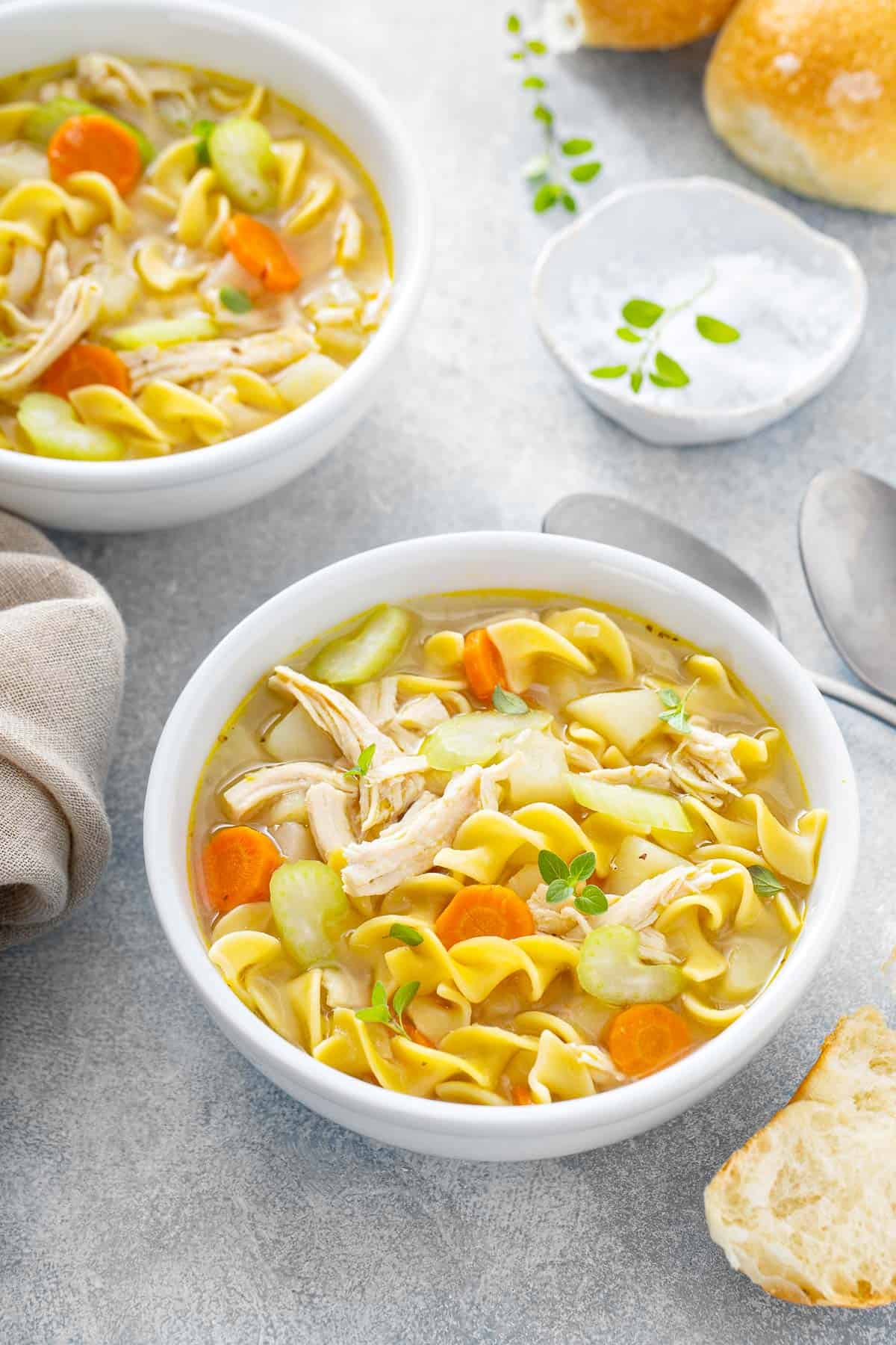 A white bowl full of soup with chicken, broth, carrots, celery, and egg noodles.