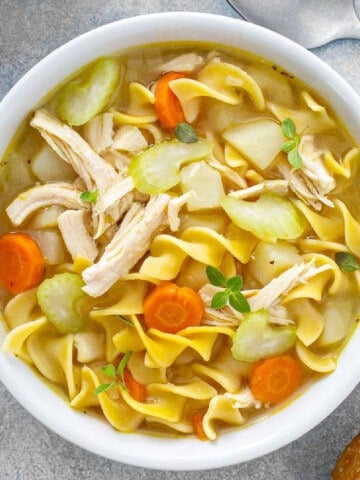 A white bowl full of soup with chicken, broth, carrots, celery, and egg noodles.