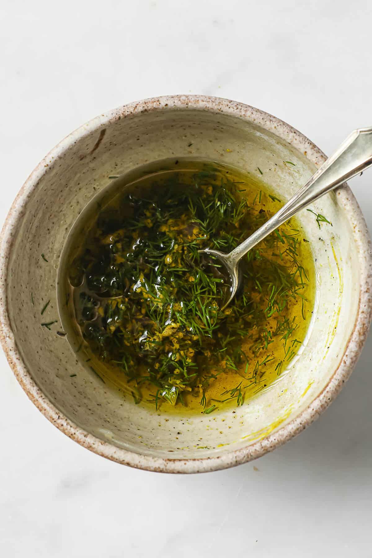 A bowl of marinade for roasted salmon - olive oil, garlic, dill, salt and pepper.