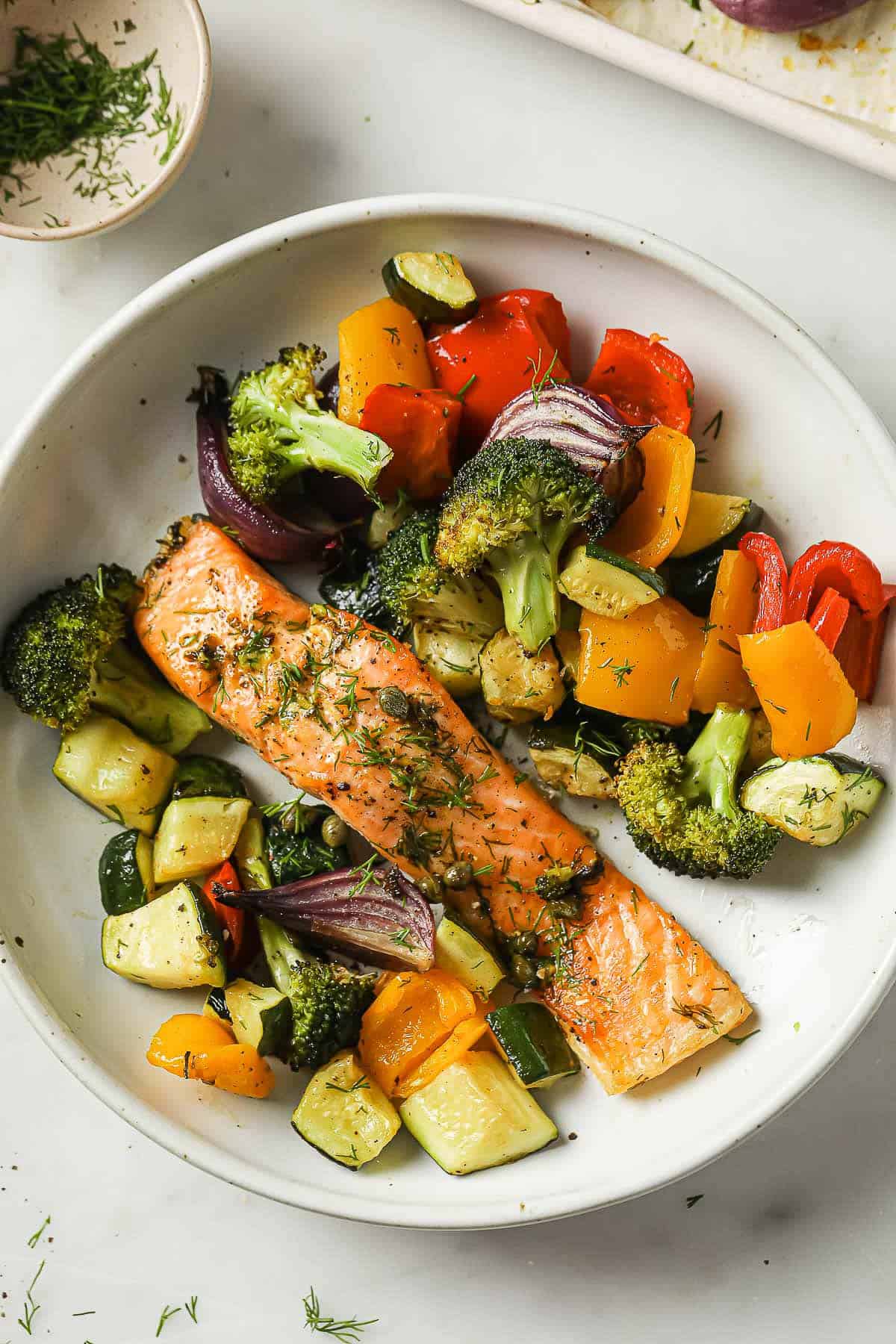 A sheet pan meal with salmon, zucchini, broccoli, red onion, peppers, capers, garlic, olive oil and spices.