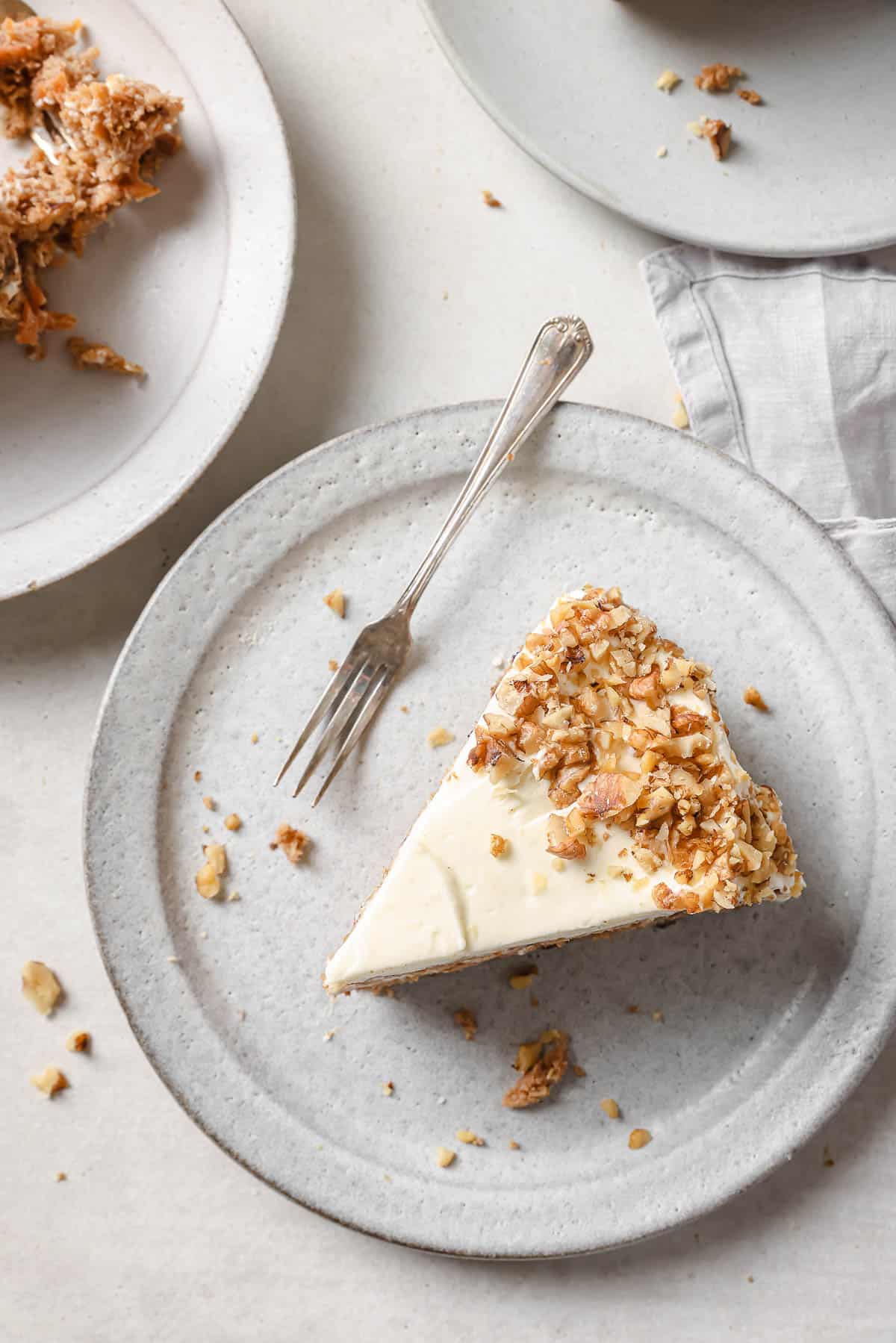 A slice of freshly baked and frosted double layer carrot cake with cream cheese frosting and toasted walnuts.