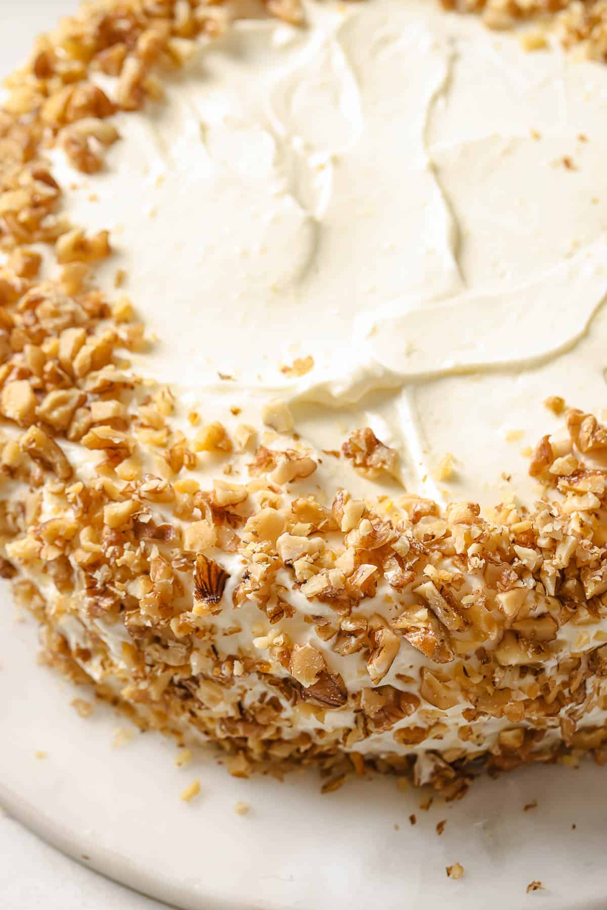 A slice of freshly baked and frosted double layer carrot cake with cream cheese frosting and toasted walnuts.