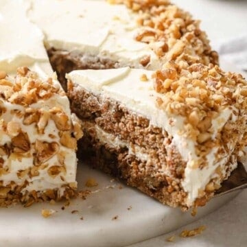 A freshly baked and frosted gluten free carrot cake, with a slice being cut from it.
