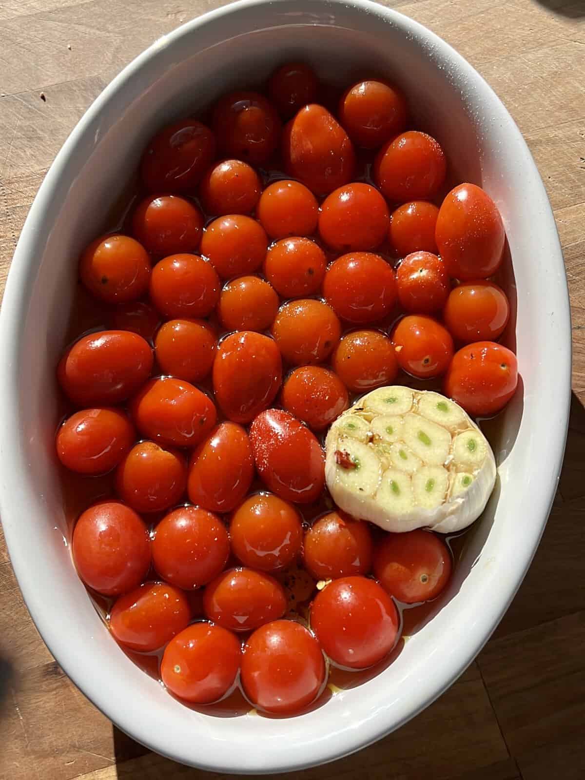 A white casserole dish with fresh grape tomatoes, garlic, olive oil, salt, and pepper.