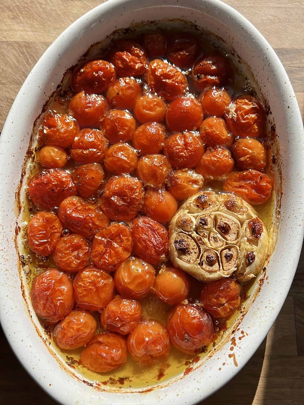 A white casserole dish with roasted tomatoes, garlic, olive oil, salt, and pepper. 