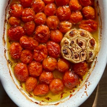 A white casserole dish with roasted tomatoes, garlic, olive oil, salt, and pepper.