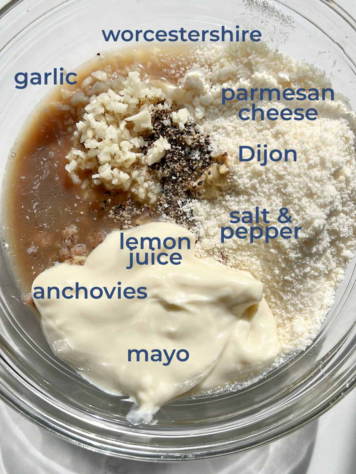 A mixing bowl with mayonnaise, garlic, lemon juice, Worcestershire sauce, salt, pepper, dijon, anchovies and garlic in it.