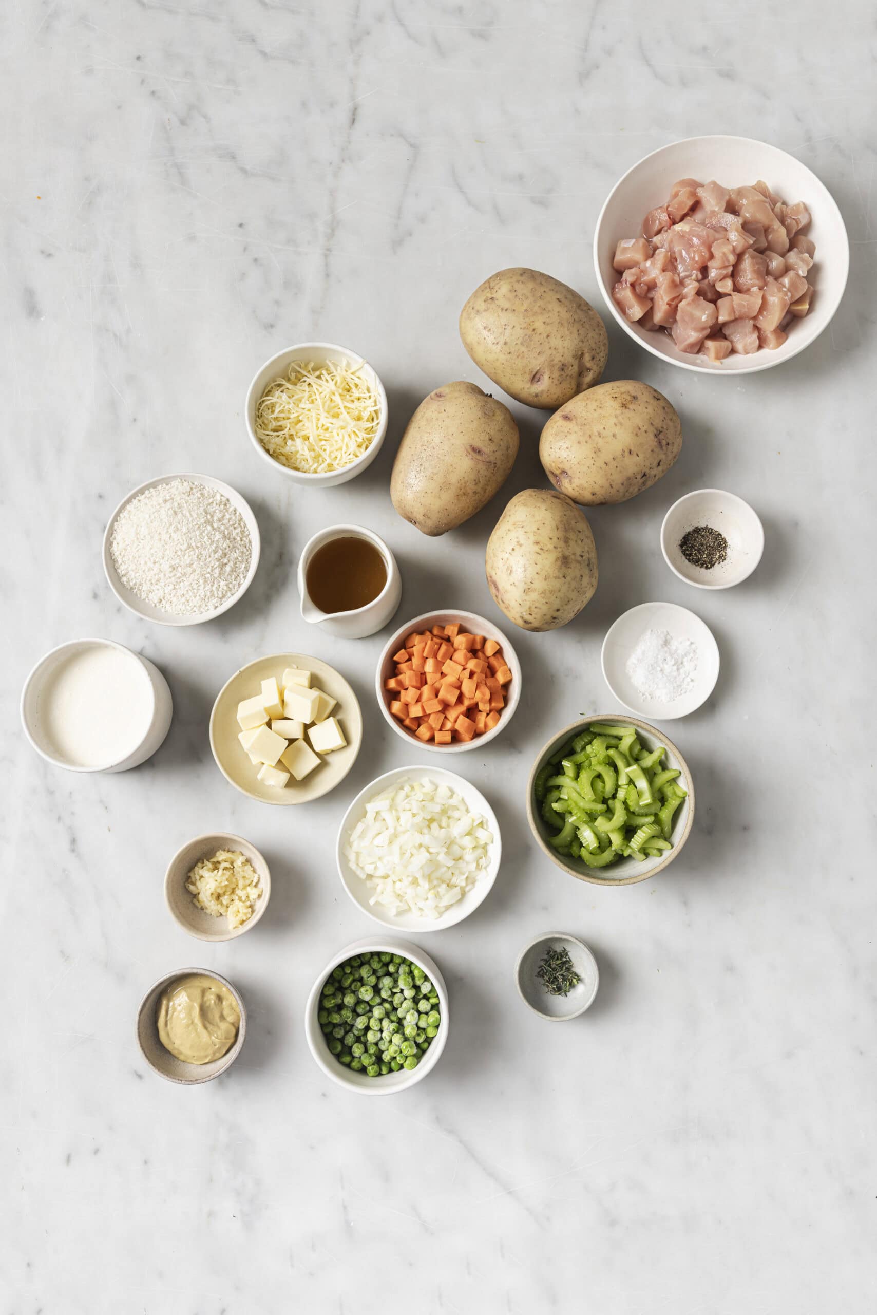 An overhead shot of fresh food ingredients laid out to begin making homemade chicken pot pie and baked potatoes.