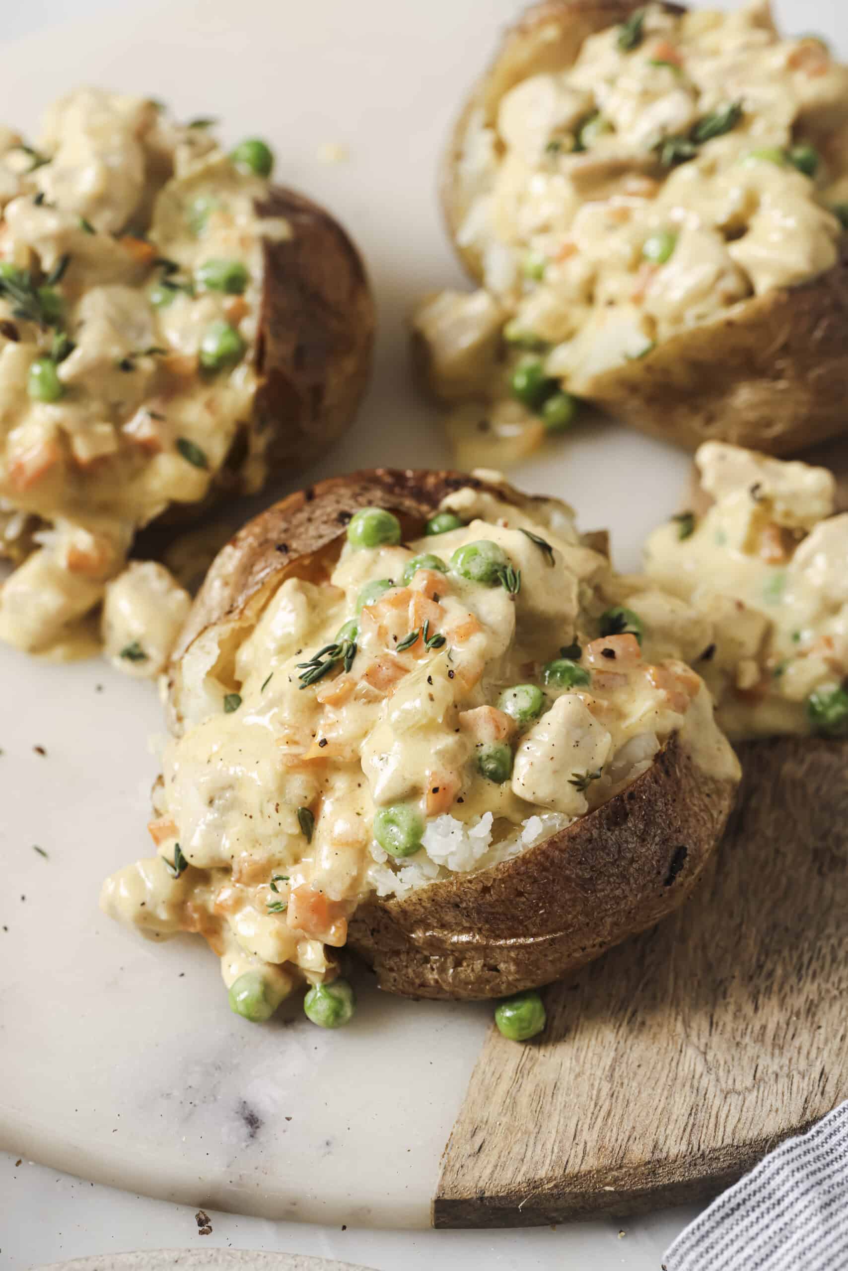 Three chicken pot pie stuffed baked potatoes ceramic plates, garnished with toasted breadcrumbs and fresh thyme.