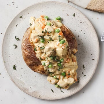 A chicken pot pie stuffed baked potato on a ceramic plate, garnished with fresh thyme.