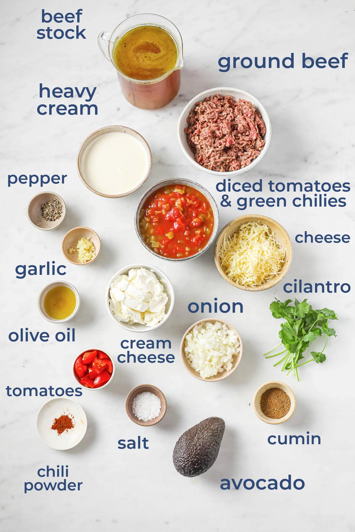 An overhead shot on ingredients laid out to make soup - ground beef, garlic, cheese, cream cheese, tomatoes, avocado, cilantro, cream, broth, and spices.