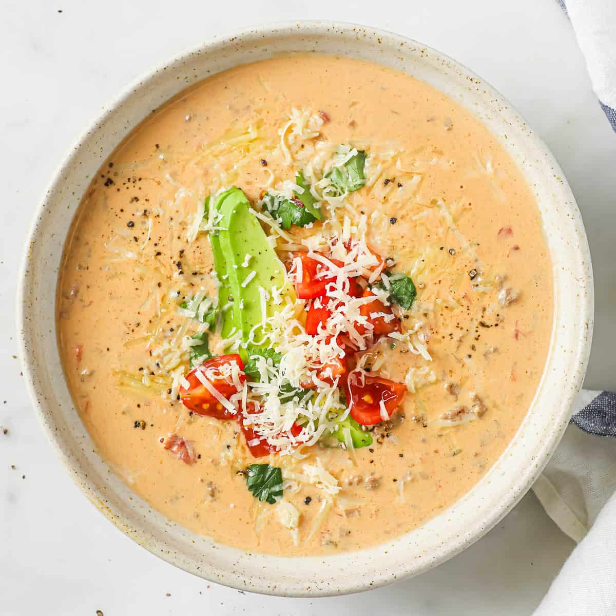 A overhead shot of bowl of creamy taco soup, garnished with avocado, tomatoes, cheese, and cilantro.