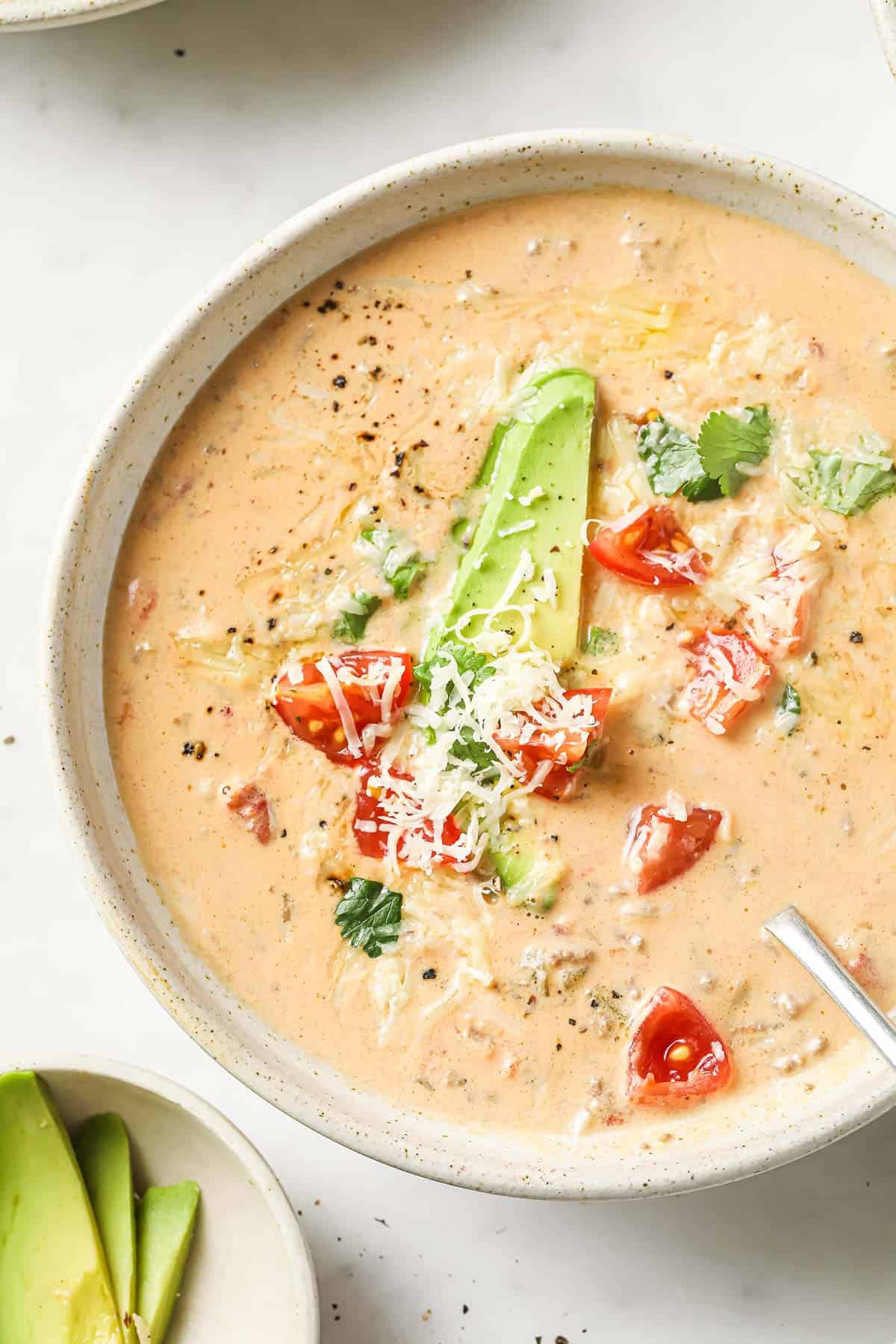 An overheat shot of a bowl of creamy taco soup, garnished with avocado, tomatoes, cheese, and cilantro.
